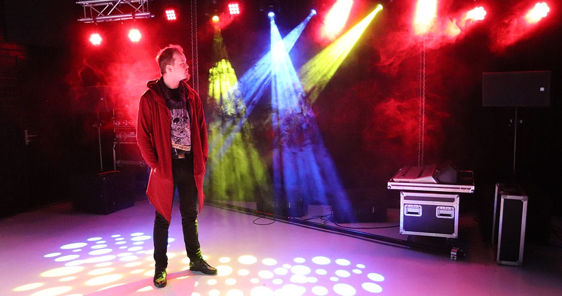 Mies seisoo esityslavalla ja katselee lavan värikkäitä valoja ja savua.