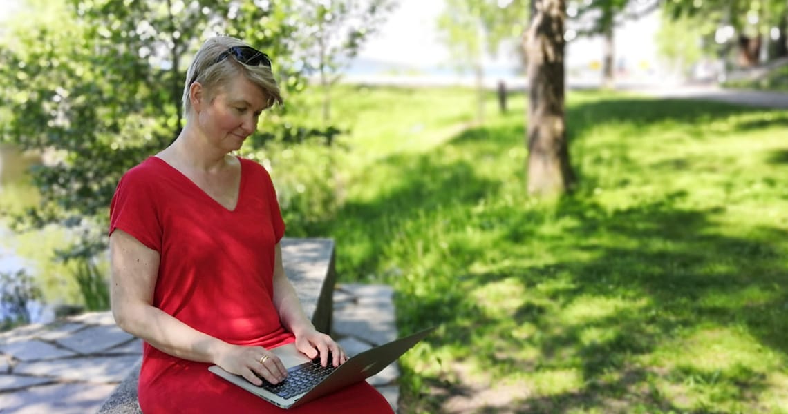 Nainen istuu puistossa tietokone sylissään.