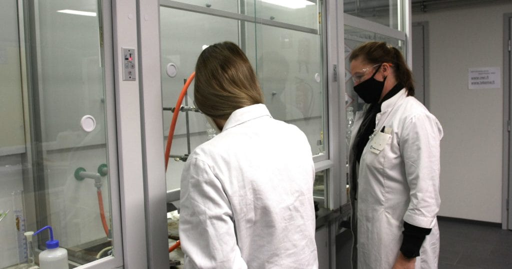 Kaksi naista laboratoriotakeissa työskentelee vetokaapin ääressä.