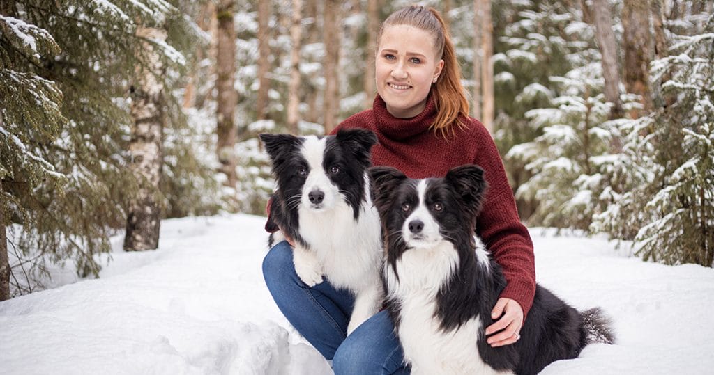 "Nainen kahden koiran kanssa ulkona lumisessa maisemassa."