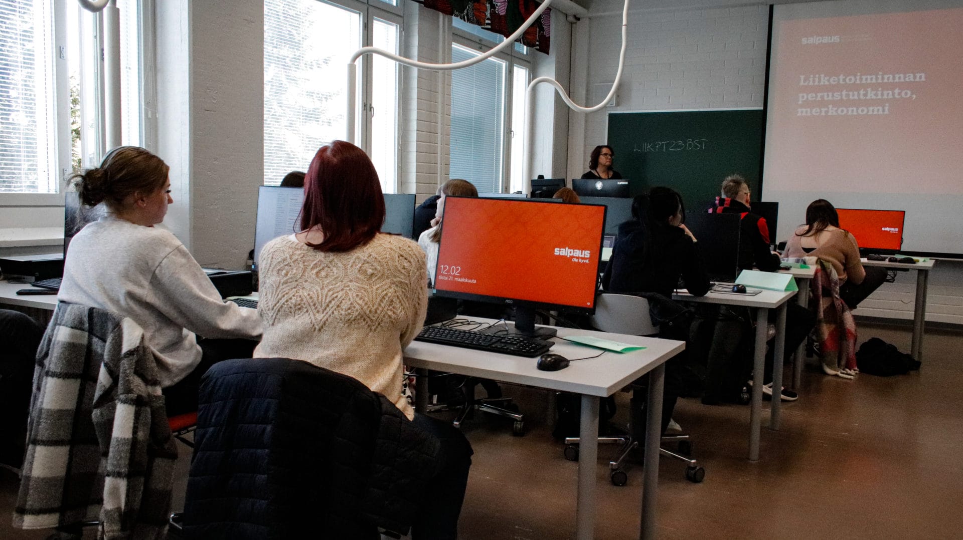 "Aikuisia opiskelijoita luokassa tietokoneen ääressä."