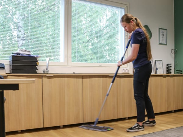 "Nainen siivoa mopilla toimiston lattiaa."